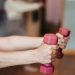 person holding pink and white dumbbells